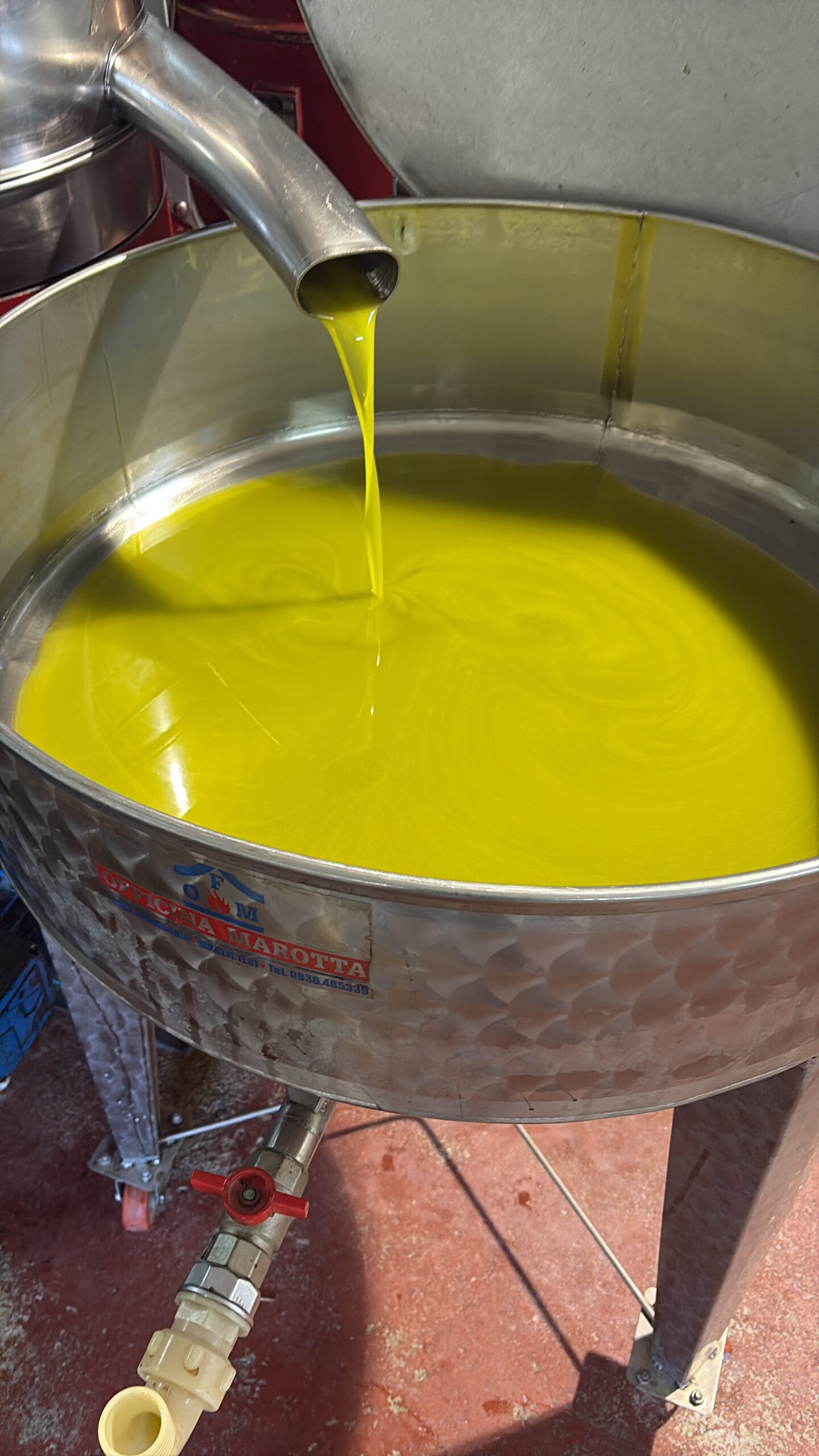 A stainless steel tank with a spout pouring bright green olive oil into a container.