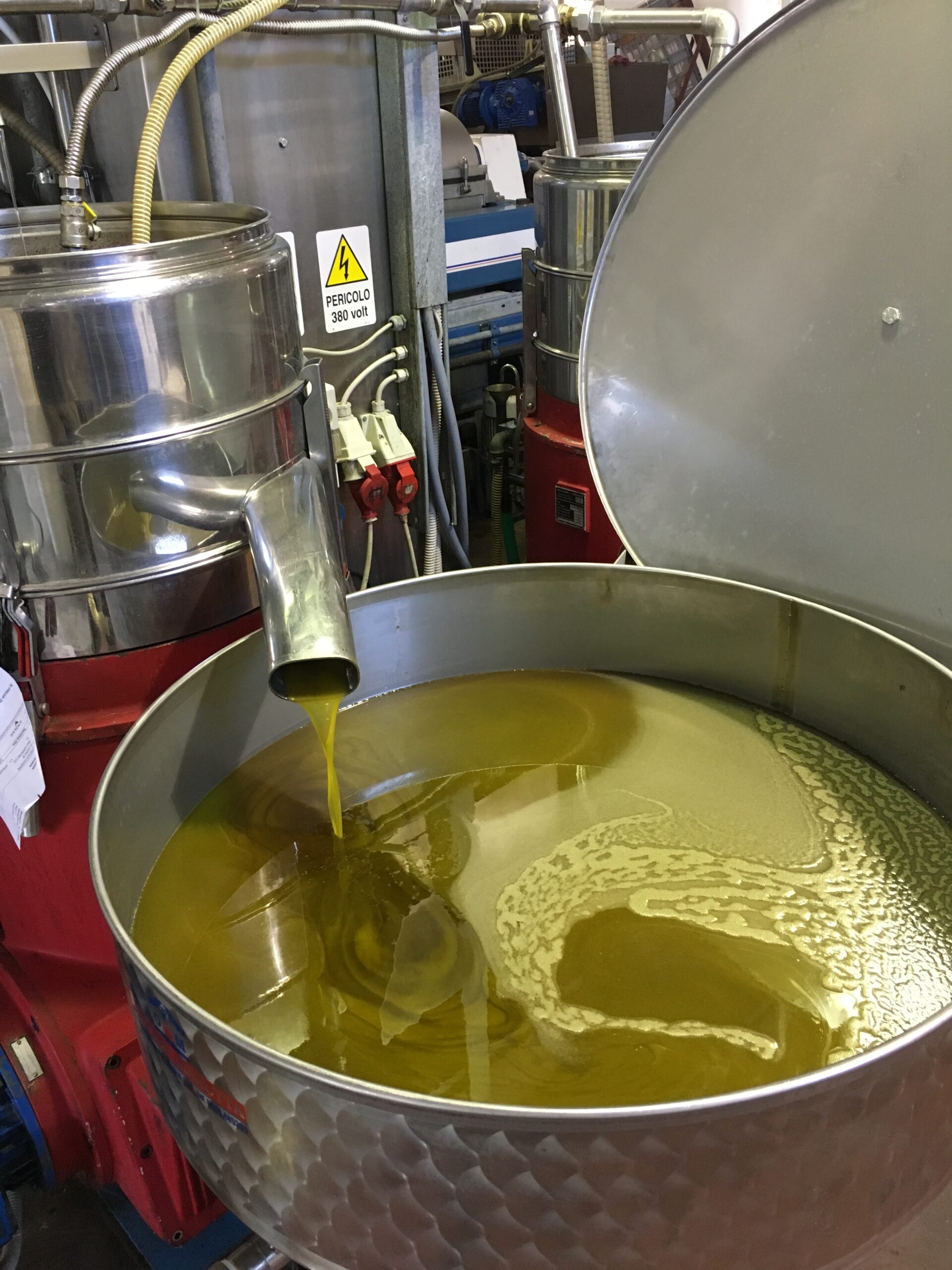 Olive oil being poured into a metal container at an oil production facility.